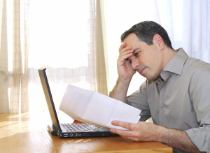 Man sitting at his desk with a laptop and bills looking concerned